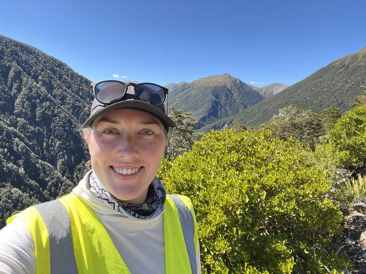 A selfie of a woman wearing hi vis, a hat and sunglasses on a hill.